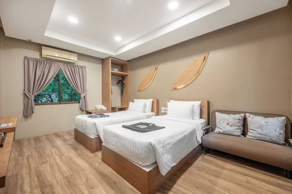 A hotel room with two beds, a sofa, a wooden wardrobe, and a window with curtains.