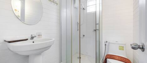 A bathroom with a glass-enclosed shower, a pedestal sink, and a toilet with a towel on it.