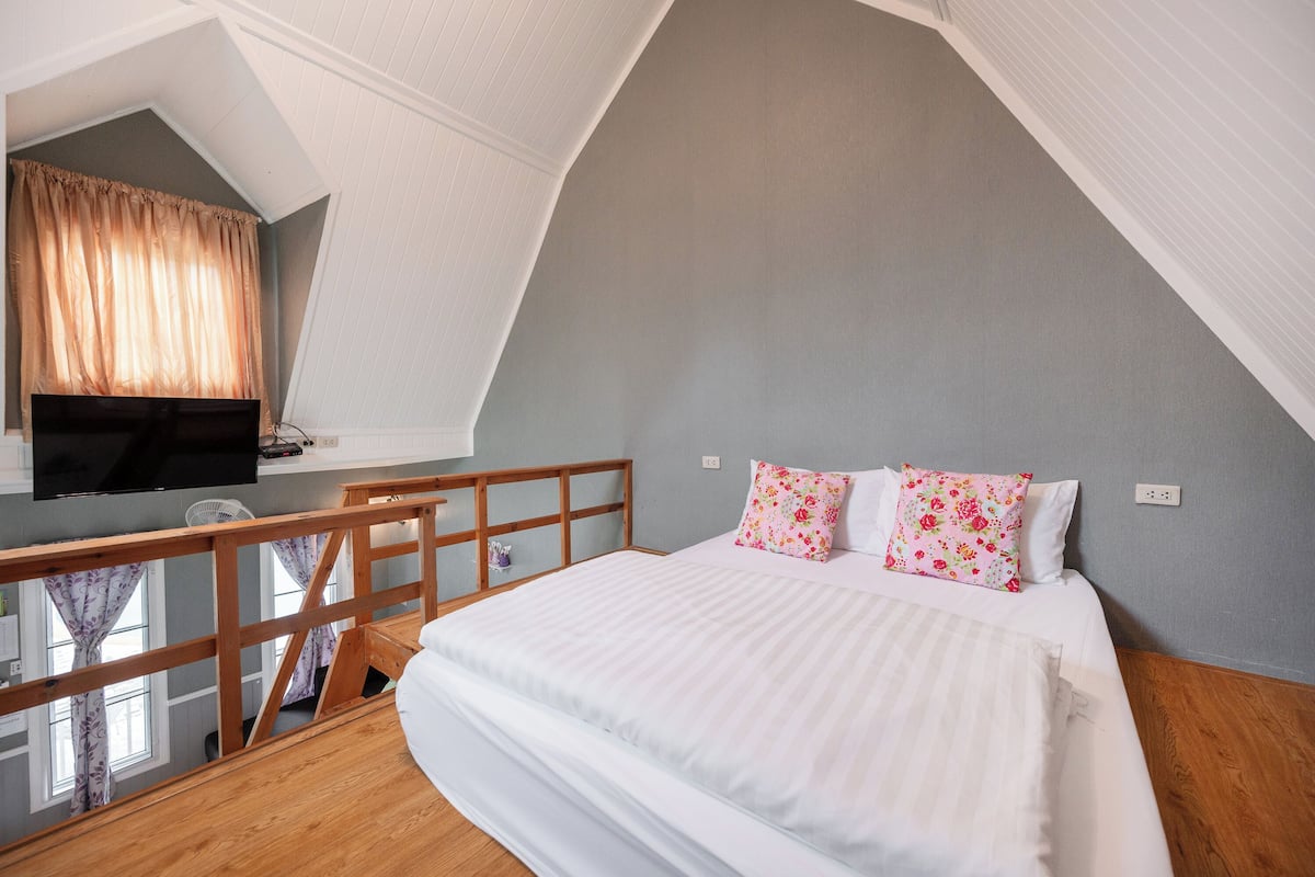 A bedroom with a bed, a TV mounted on the wall, and a balcony with a wooden railing.