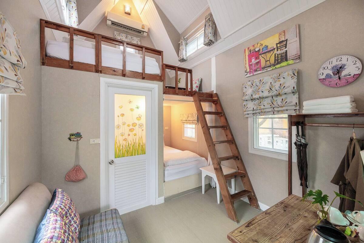 A cozy room with a bunk bed, a ladder, a small table with a plant, and a wall clock.