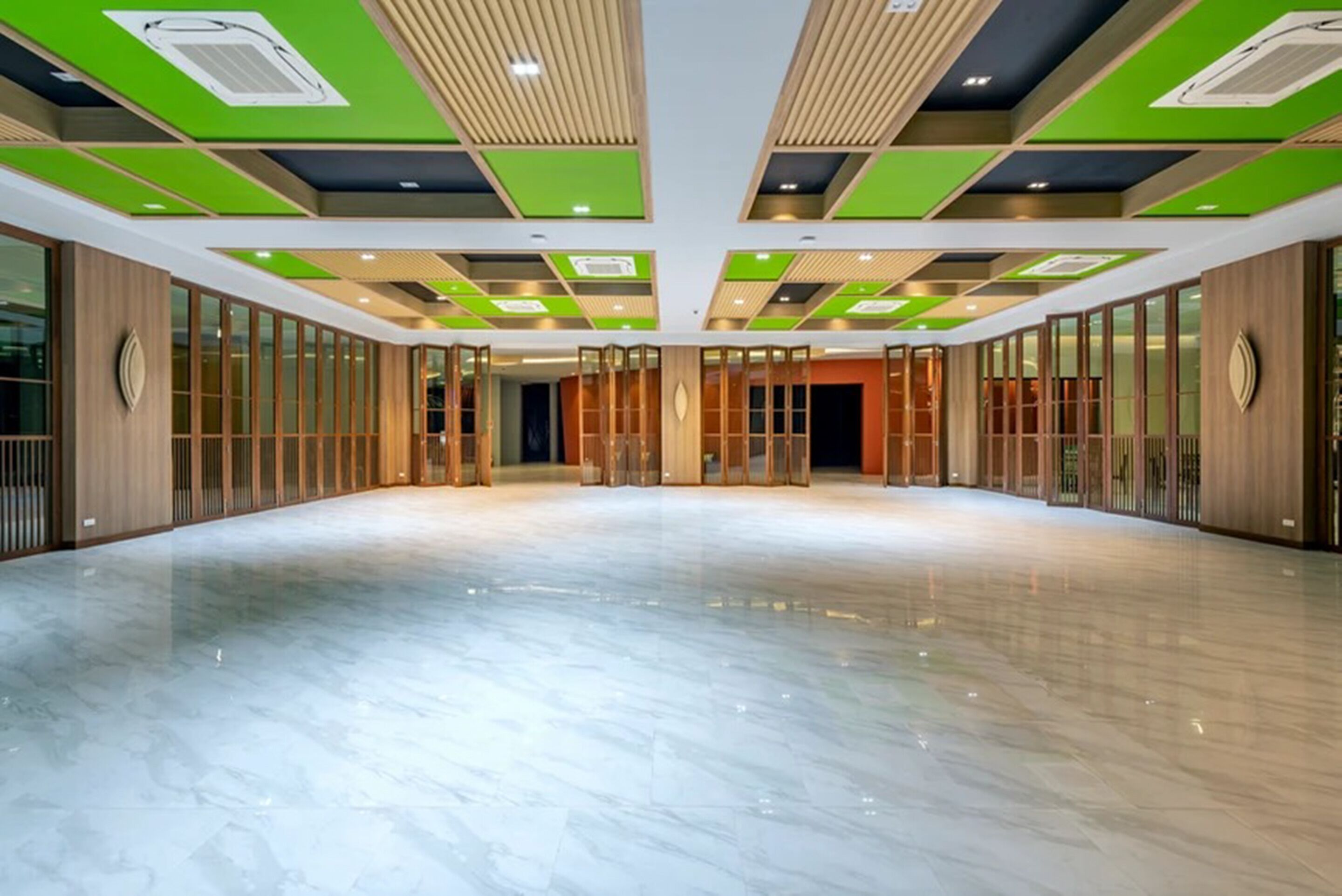 Eine großzügige, moderne Hotelhalle mit glänzendem Marmorboden, grünen und beigen Deckenpaneelen und Holzakzenten.