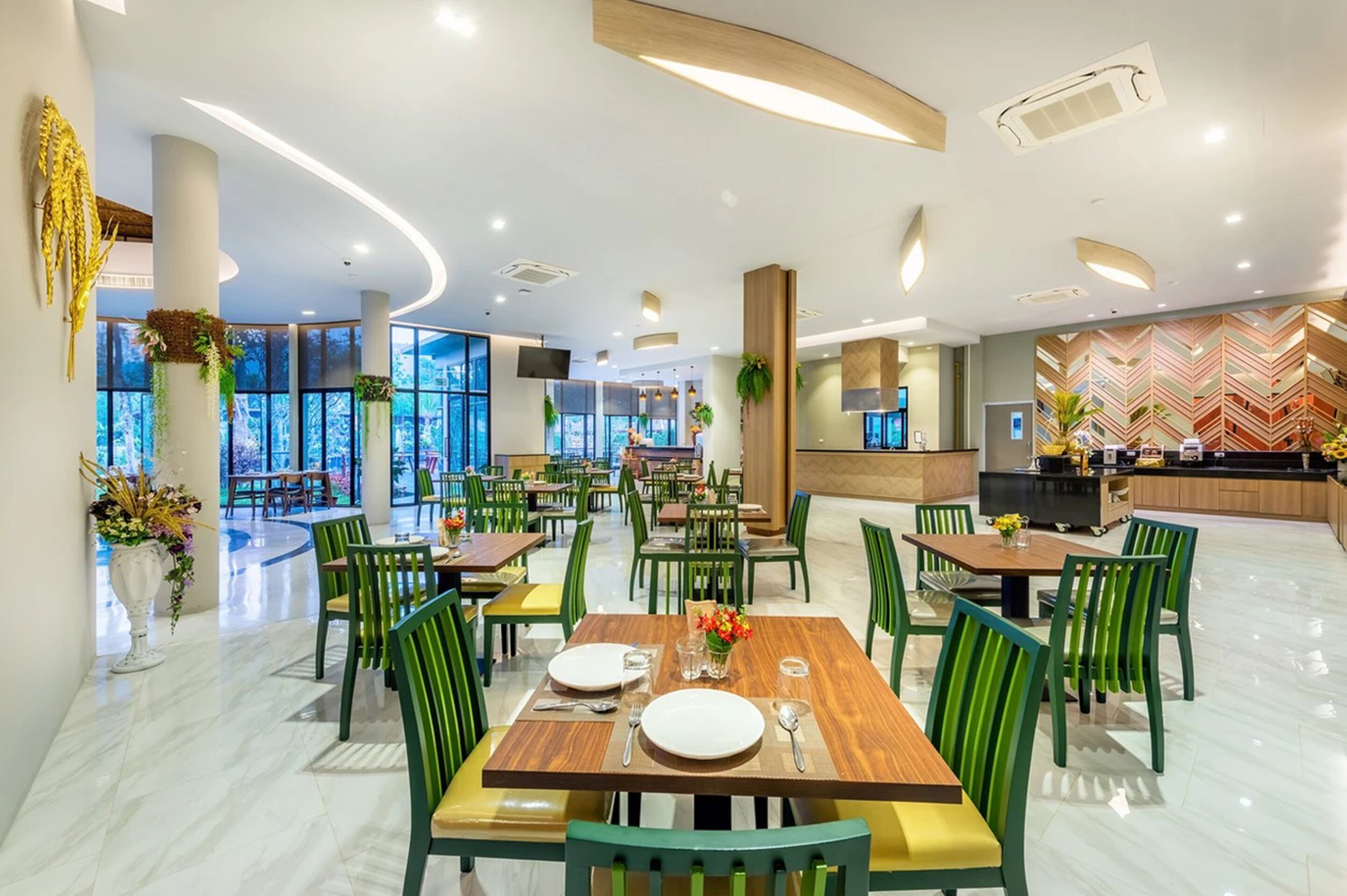 Un espace repas moderne avec plusieurs tables et chaises, de grandes fenêtres et une cuisine en arrière-plan.