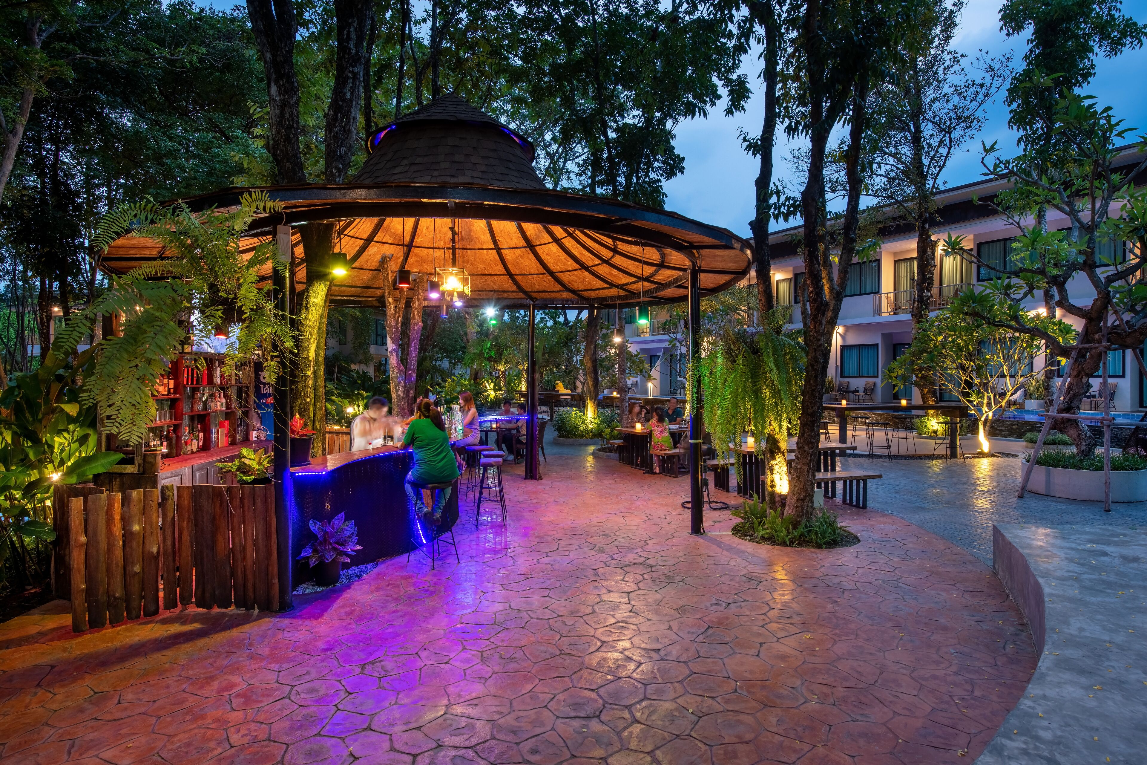 Un patio al aire libre con un quiosco de madera, zonas de estar y una barra con un letrero de neón.