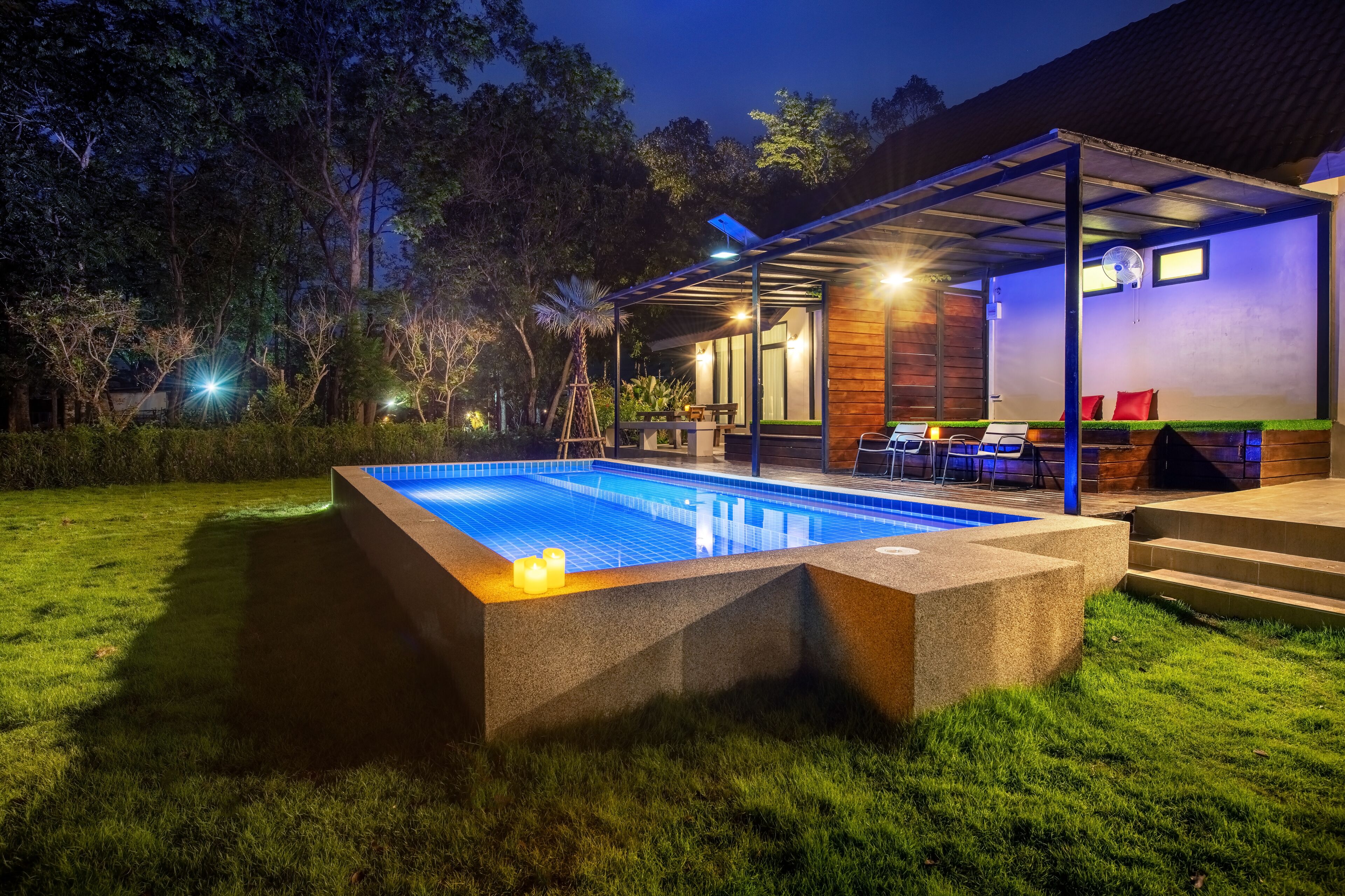 A swimming pool with a wooden deck, surrounded by a well-maintained lawn and trees.