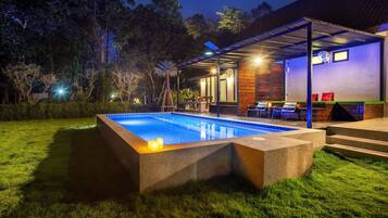 A swimming pool with a wooden deck, surrounded by a well-maintained lawn and trees.