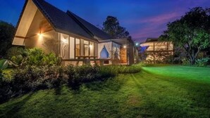 Una casa moderna con un'ampia vetrata, un prato curato e un cielo sereno al crepuscolo.