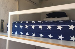Un lit superposé avec un matelas bleu orné de motifs en forme d’étoiles blanches, une structure blanche et un oreiller noir sur le dessus.