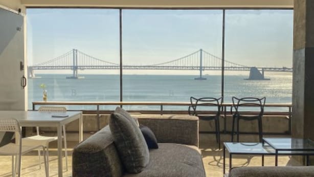 Een balkon met uitzicht op een brug over het water, voorzien van een bank, stoelen en een tafel.