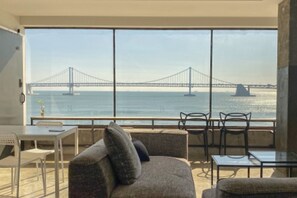 Un balcon donnant sur un pont enjambant une étendue d’eau, aménagé avec un canapé, des fauteuils et une table.