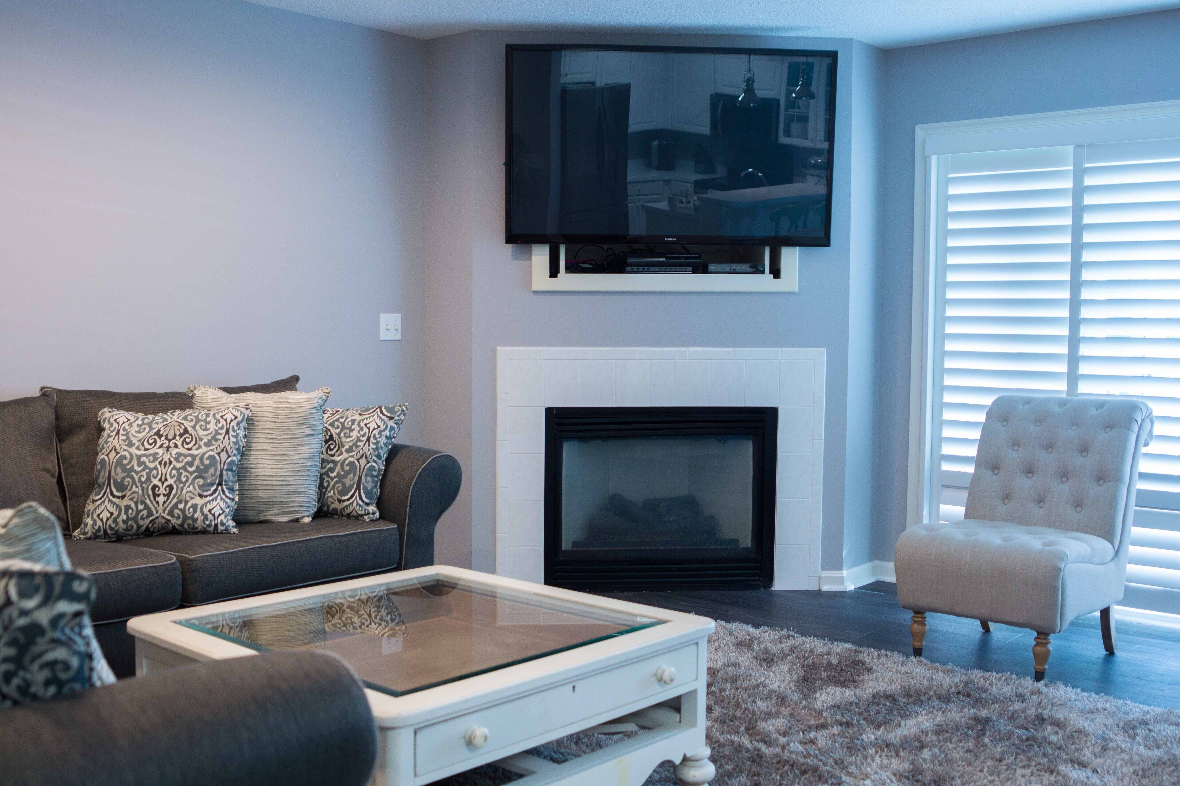 Una sala de estar con sofá, sillón, chimenea y televisor de pantalla plana montado sobre la chimenea.