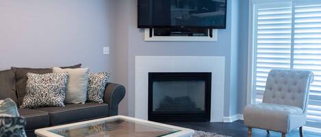 Una sala de estar con sofá, sillón, chimenea y televisor de pantalla plana montado sobre la chimenea.