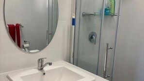 Bathroom features a sink, round mirror, and glass-enclosed shower with showerhead and soap dispenser.