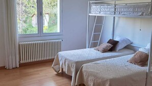 Een slaapkamer met twee eenpersoonsbedden, een raam, een radiator en een ladder.