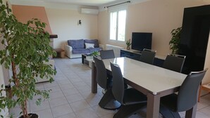 Een moderne woonkamer met een eethoek, een bank, een televisie en een potplant.