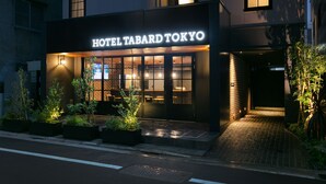 The exterior of Hotel Tabard Tokyo with illuminated signage, a brick facade, and a well-lit entrance. - Hotel Tabard Tokyo (Tokyo)