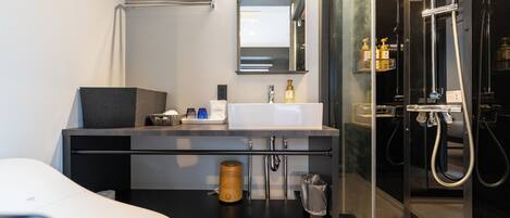Un baño moderno con un lavamanos blanco, un espejo, un perchero para toallas, una cabina de ducha y un inodoro.