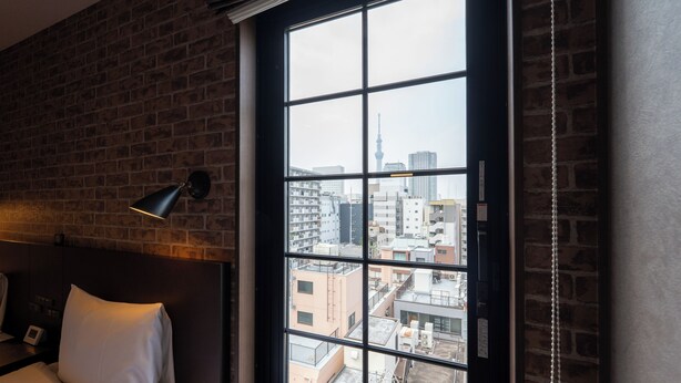 A hotel room with a large window, a brick wall, a bed with white bedding, and a black lamp on the nightstand. - Hotel Tabard Tokyo (Tokyo)
