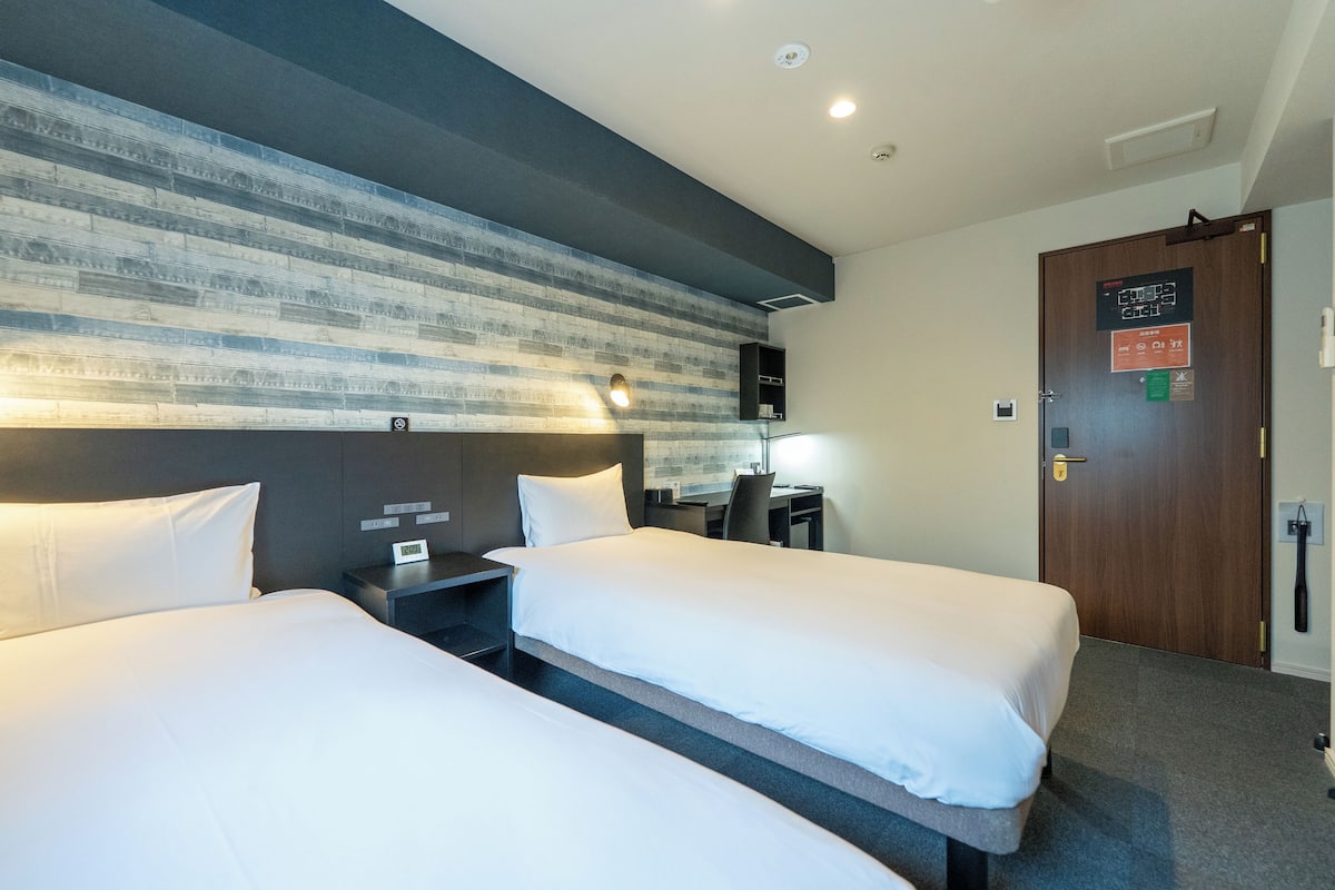 Een hotelkamer met twee bedden, een bureau, een stoel en een tv aan de muur.