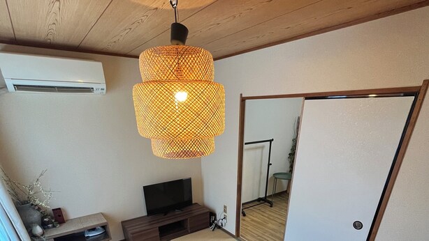 A living room with tatami flooring, a sofa, a coffee table, a TV, and a hanging lamp. - EX Tenjinnomori Apartment 202 (Osaka)