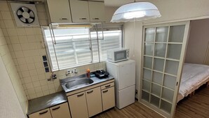 A compact kitchen with a microwave, sink, and cabinets. There's a small refrigerator and a window with blinds. - EX Tenjinnomori Apartment 202 (Osaka)