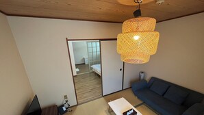 A room with a sofa, a small table, a lamp, a TV, and a sliding door leading to a bedroom. - EX Tenjinnomori Apartment 202 (Osaka)