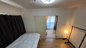 A hotel room with a bed, wooden flooring, a standing lamp, and a view through a door to a balcony. - EX Tenjinnomori Apartment 202 (Osaka)