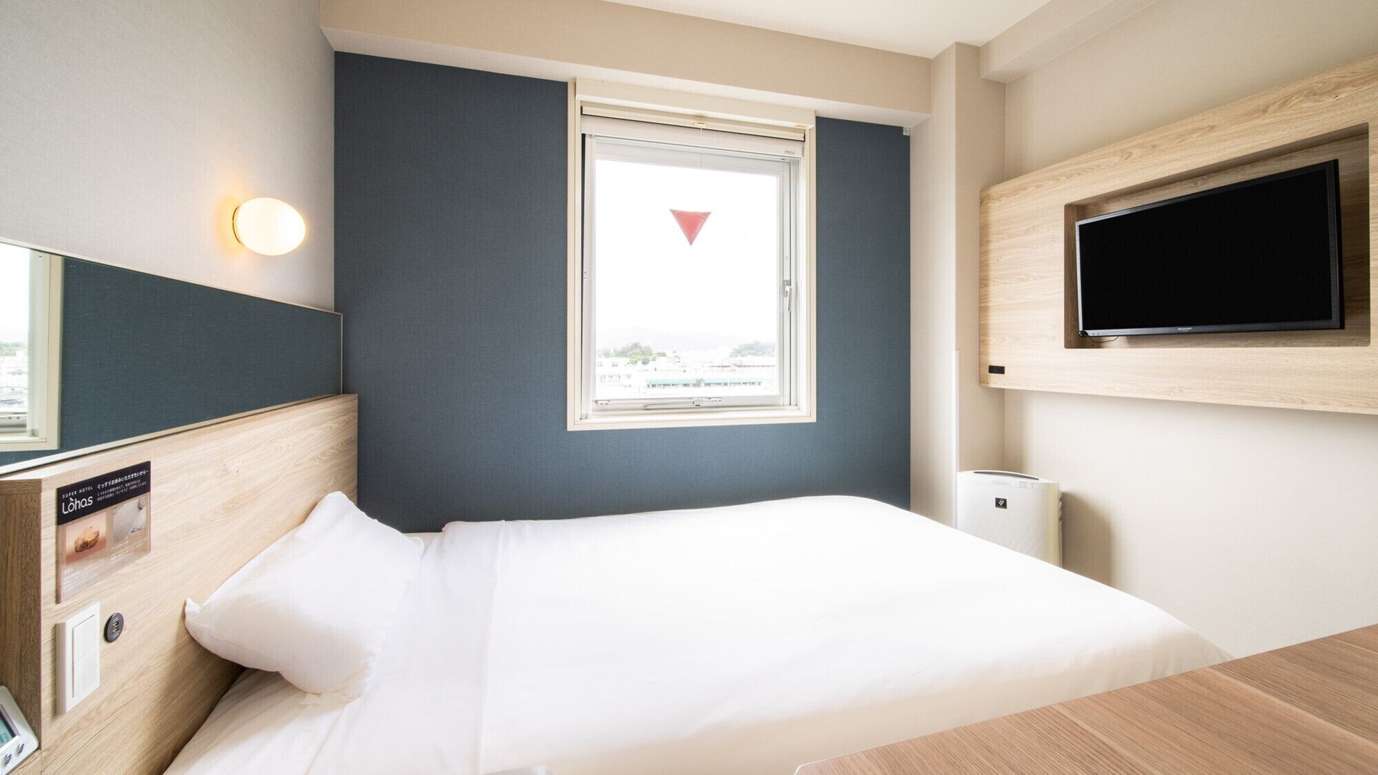 Quarto de hotel com cama, televisão fixada na parede, janela com vista e termostato na parede.