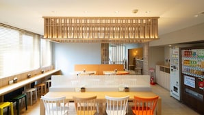 A modern cafe with wooden furniture, a central seating area, and a vending machine.