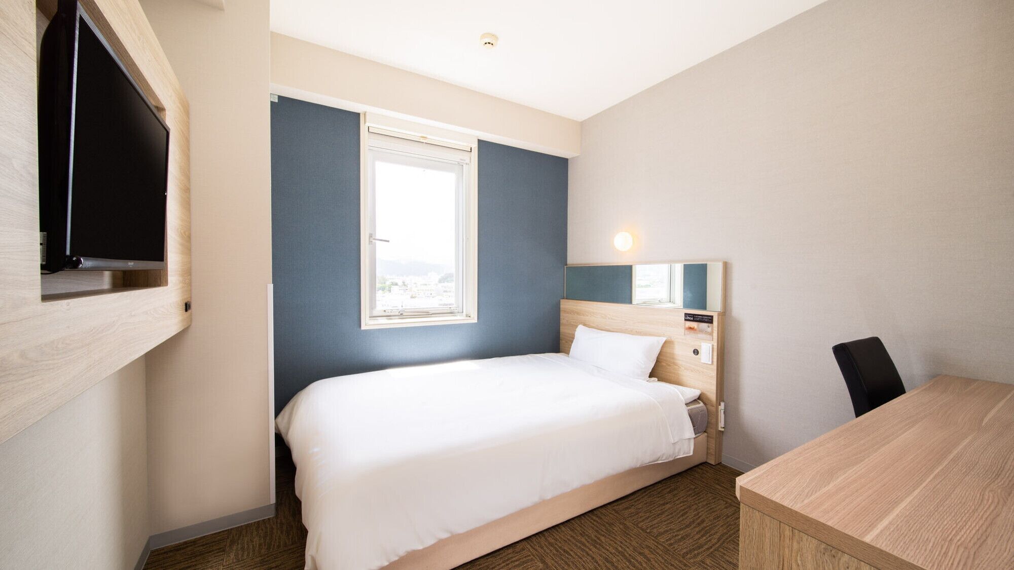 Quarto de hotel com cama, escrivaninha, televisão e janela.
