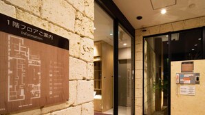 A hotel lobby with a stone wall, a map of the hotel layout, and a reception desk with a glass partition.
