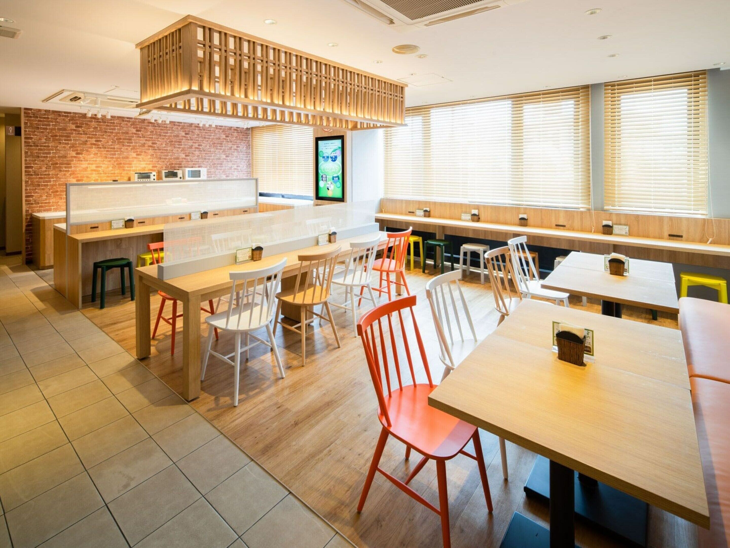 Een modern café met houten tafels en stoelen, een bakstenen muur en grote ramen.