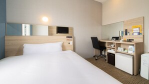 A hotel room with a large bed, a desk with a chair, a small refrigerator, and a mirror on the wall.