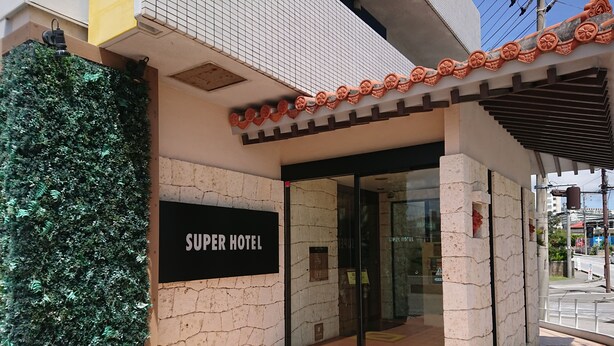 The exterior of a hotel with a sign reading "SUPER HOTEL," a glass entrance, and a tiled walkway.