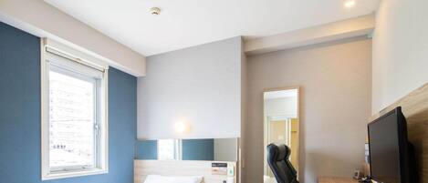 A hotel room with a bed, a desk, a chair, a television, and a window.