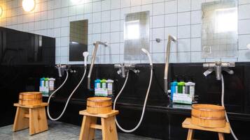 A public restroom with three wooden stools, a black tiled wall, and multiple hand dryers.