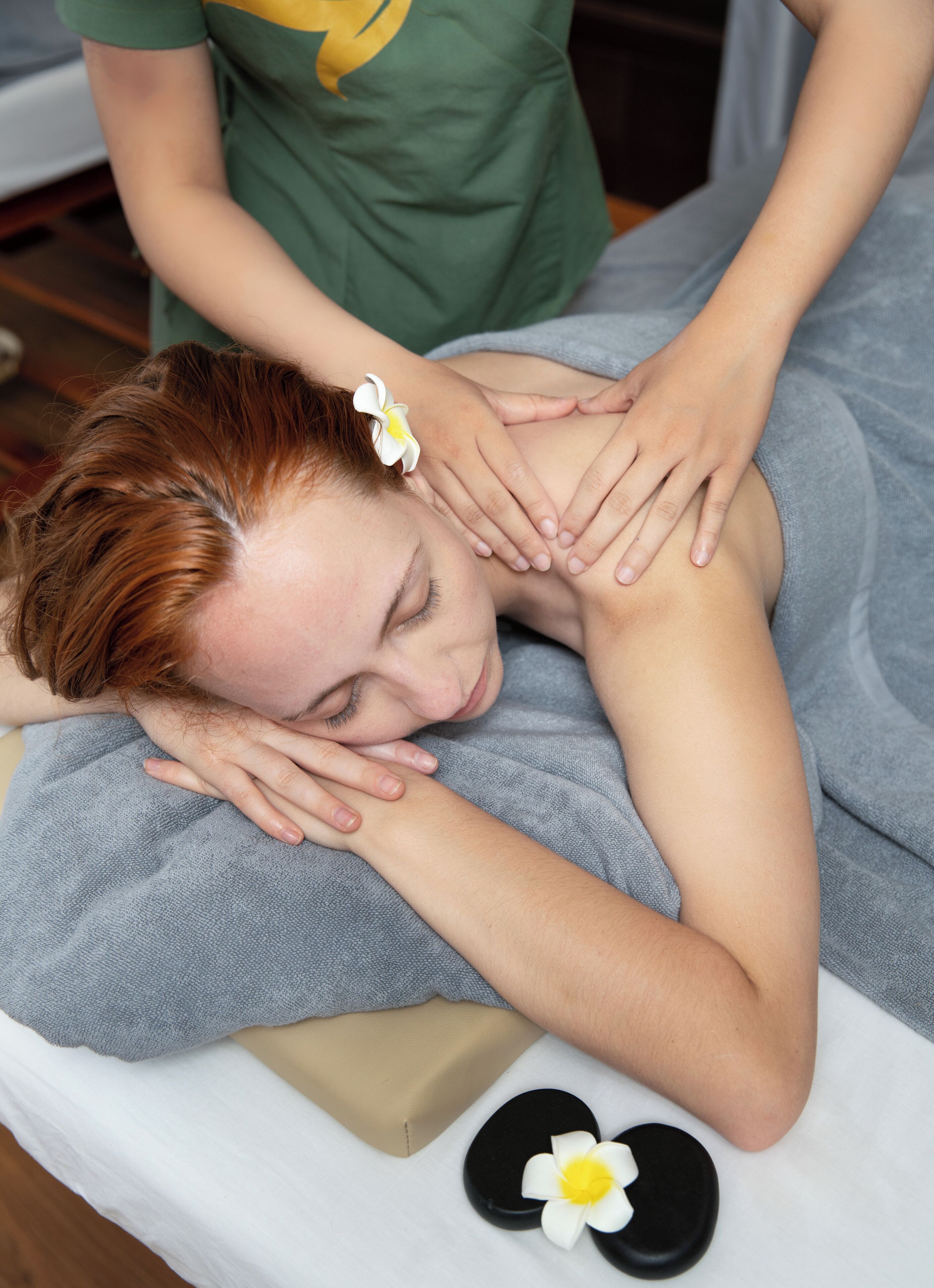 Eine Person erhält eine Massage auf einer Liege, mit Handtuch und Blumenblumen.