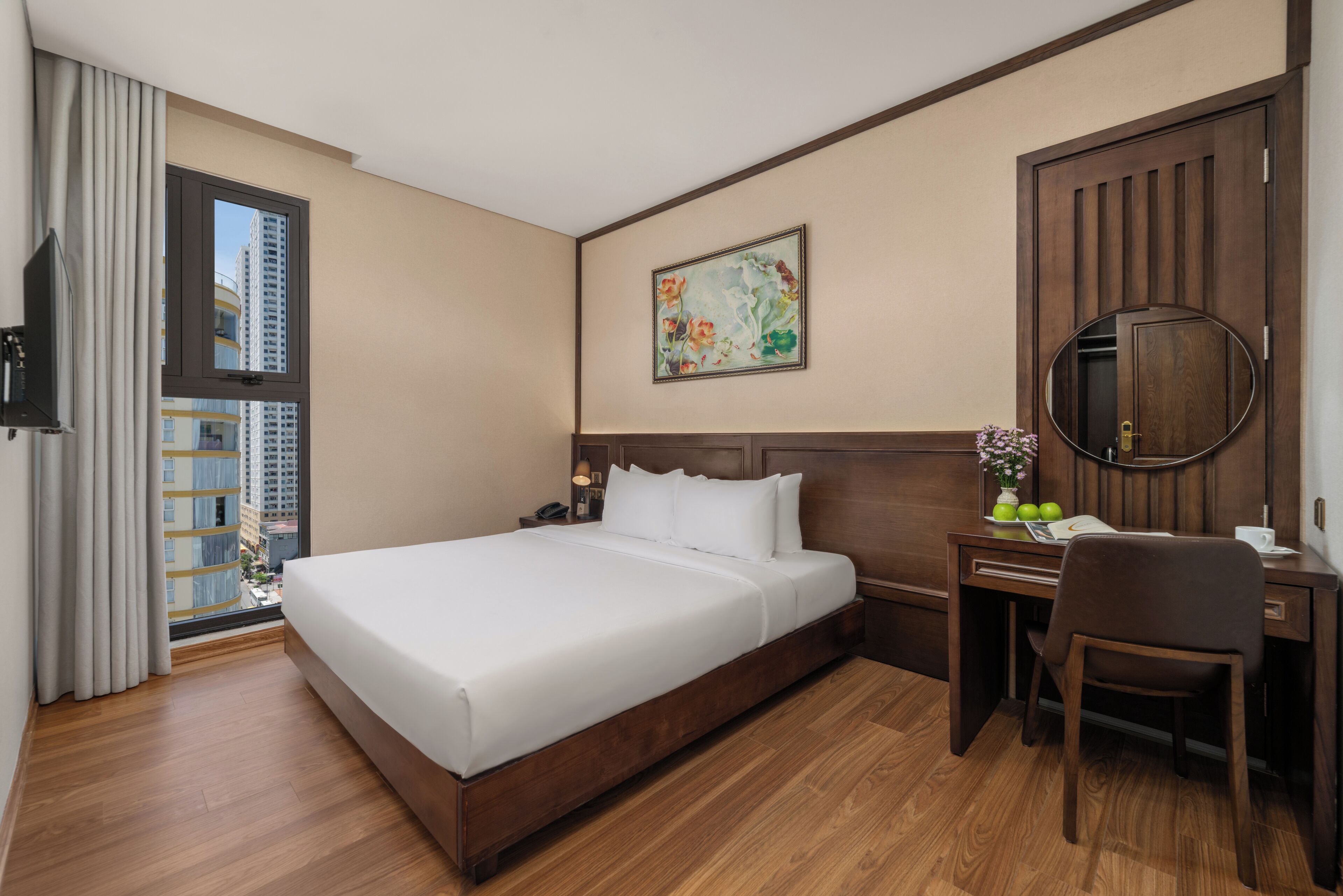 A hotel room with a large bed, a desk with a chair, a TV, and a window with curtains.
