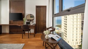 A modern hotel room with a wooden desk, a flat-screen TV, a dining area with a table and chairs, and a large window offering a city view. - Golden Lotus Hotel Da Nang (Da Nang)