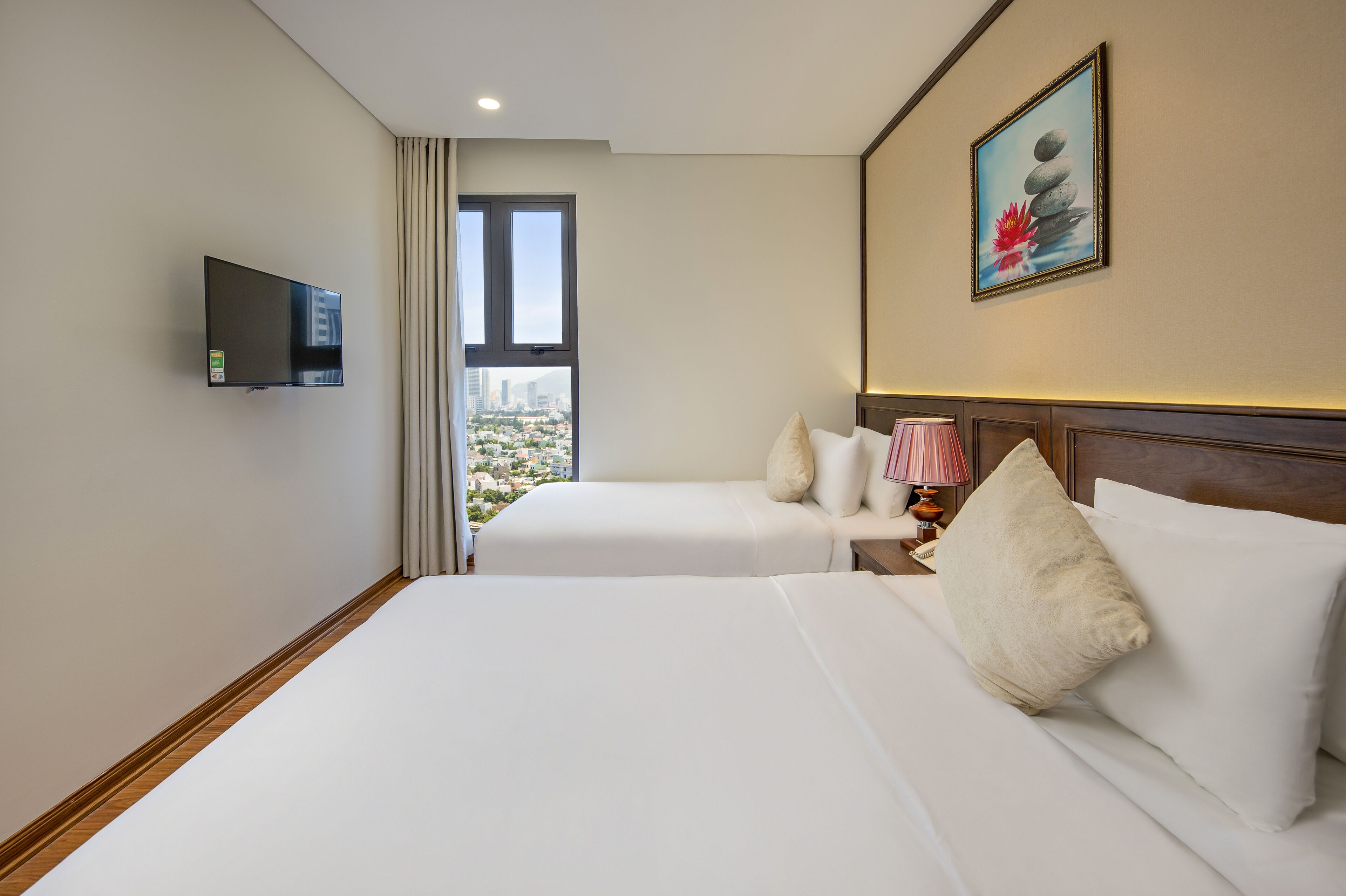 A hotel room with two beds, a TV, a window with a city view, and a painting on the wall.