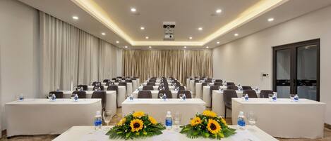 Une salle de conférence avec des rangées de tables, chacune étant agrémentée de bouteilles d’eau, de verres et de tournesols.