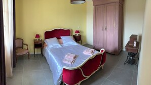 A bed with a red headboard, a wooden nightstand with a lamp, a chair, a wardrobe, and a sewing machine table.