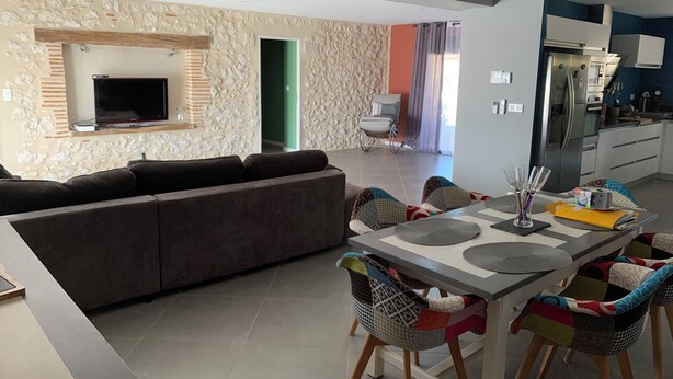 A modern living room with a sofa, a TV, and a dining area with chairs and a table.