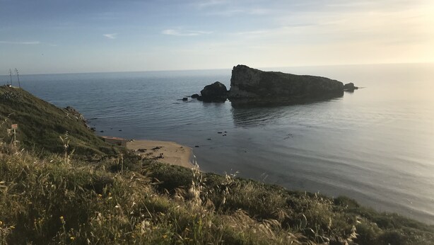 A coastal landscape with a prominent rock formation, a sandy beach, and a grassy hill. - Villa Falaride on the sea of Licata  (Licata)