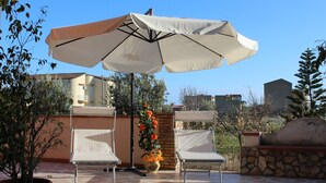 An outdoor patio with two white chairs, a large umbrella, and a potted plant with orange flowers. - Villa Falaride on the sea of Licata  (Licata)