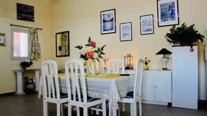 A dining area with a table set for four, surrounded by white chairs, a floral centerpiece, and framed pictures on the wall. - Villa Falaride on the sea of Licata  (Licata)