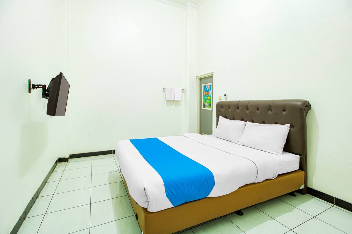 Ein ordentlich bezogenes Bett mit einer blau-weißen Tagesdecke, einem braunen Kopfteil und weißen Kissen.