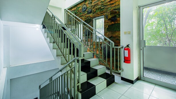 Un escalier avec une rampe en métal, un mur en pierre et un extincteur près d’une porte.