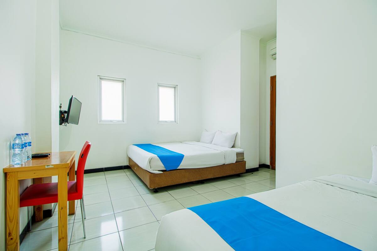 Ein Hotelzimmer mit Bett, Schreibtisch mit Stuhl, zwei Fenstern und einer Tür.