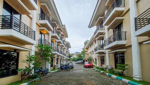A residential building with multiple balconies, a cobblestone street, and parked vehicles. - Plaza 68 Residence (Jakarta)