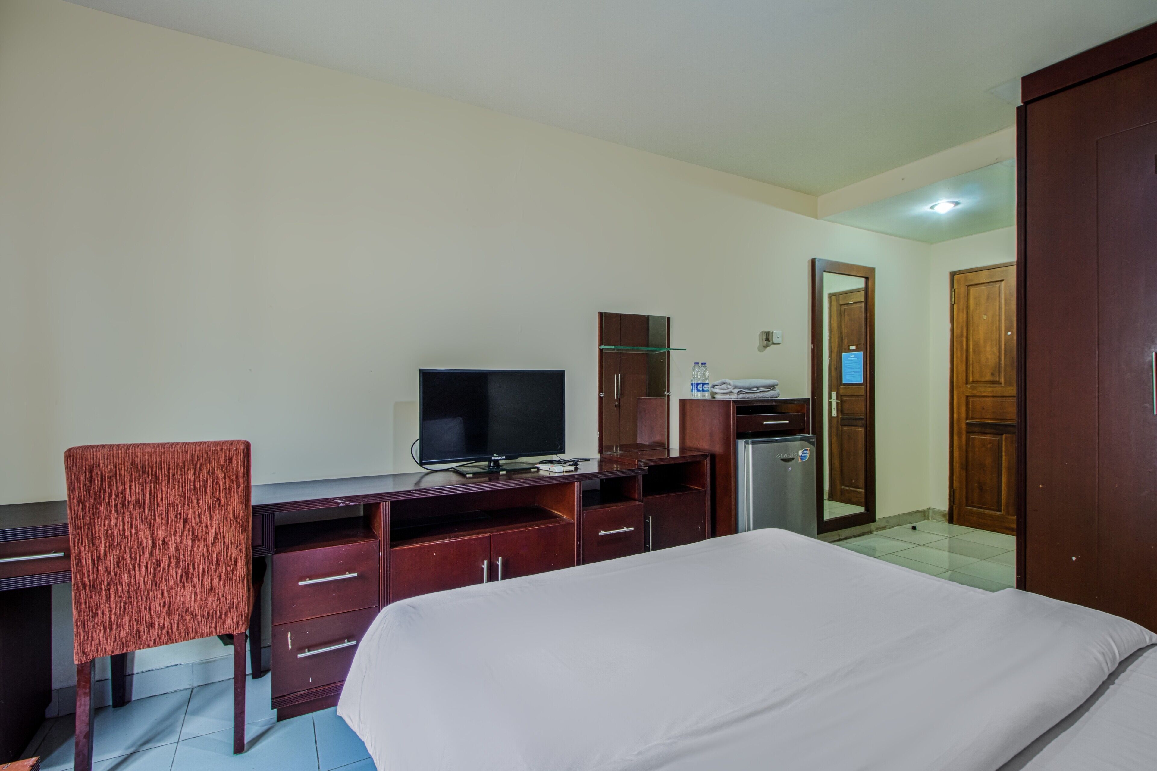 A hotel room with a bed, a desk with a television, a chair, and a wardrobe.